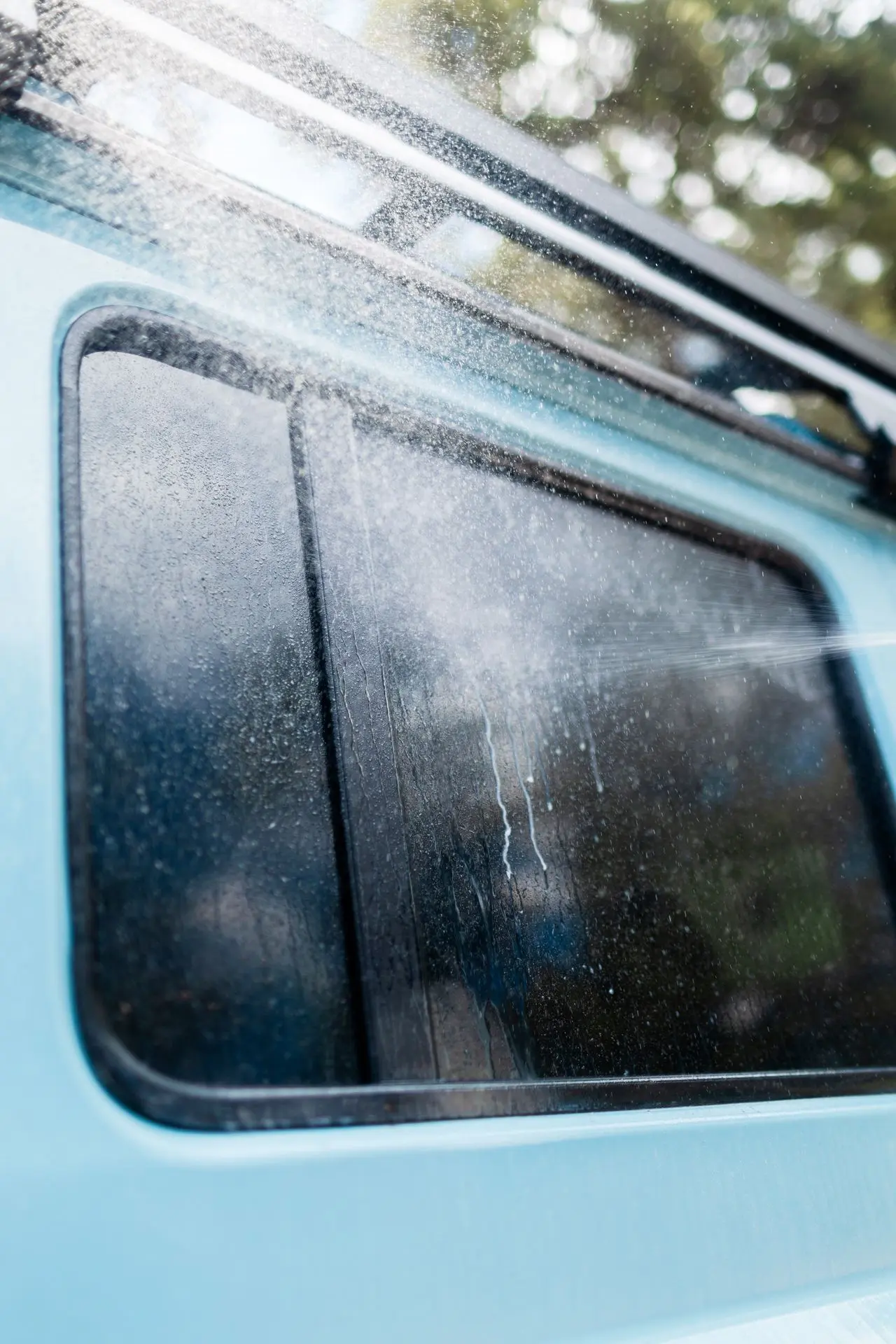 Sproeien van EcoWash-oplossing op de ramen van een blauwe 4x4