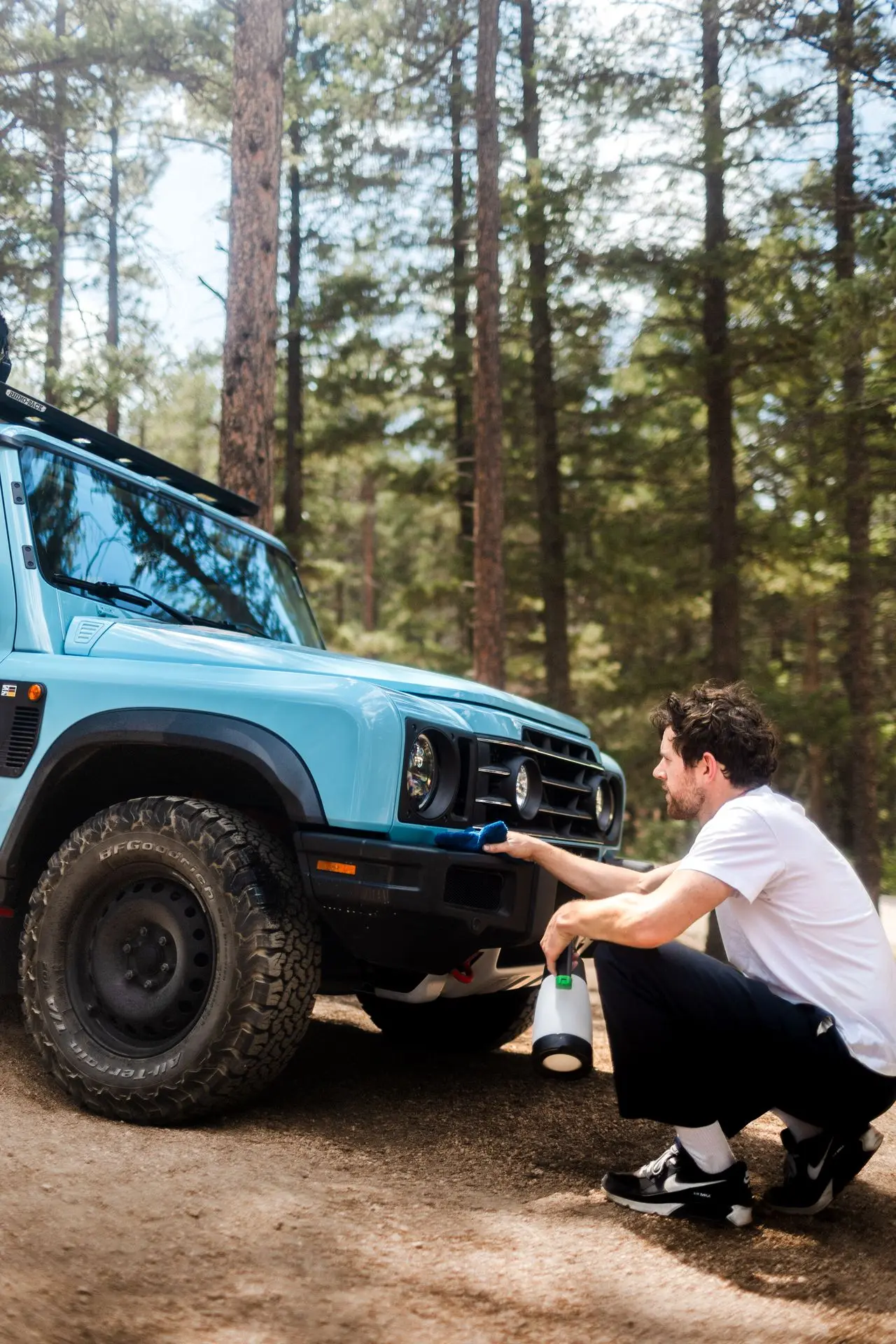 Man reinigt de voorbumper van een blauwe 4x4 in het bos met EcoWash